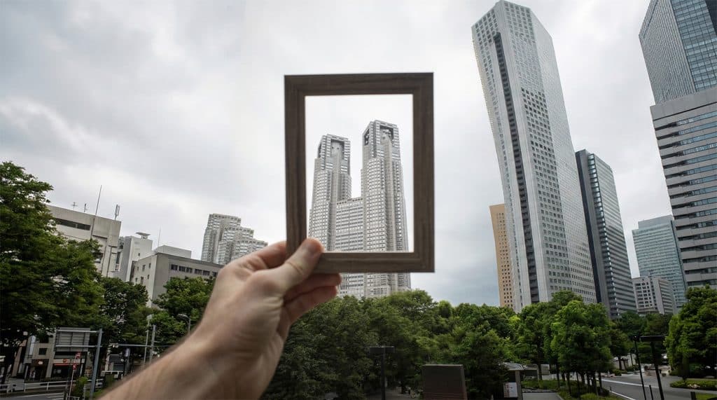 Mão segurando uma moldura que enquadra um arranha-céu corporativo, simbolizando o foco estratégico na sinergia entre direito imobiliário e tributário.